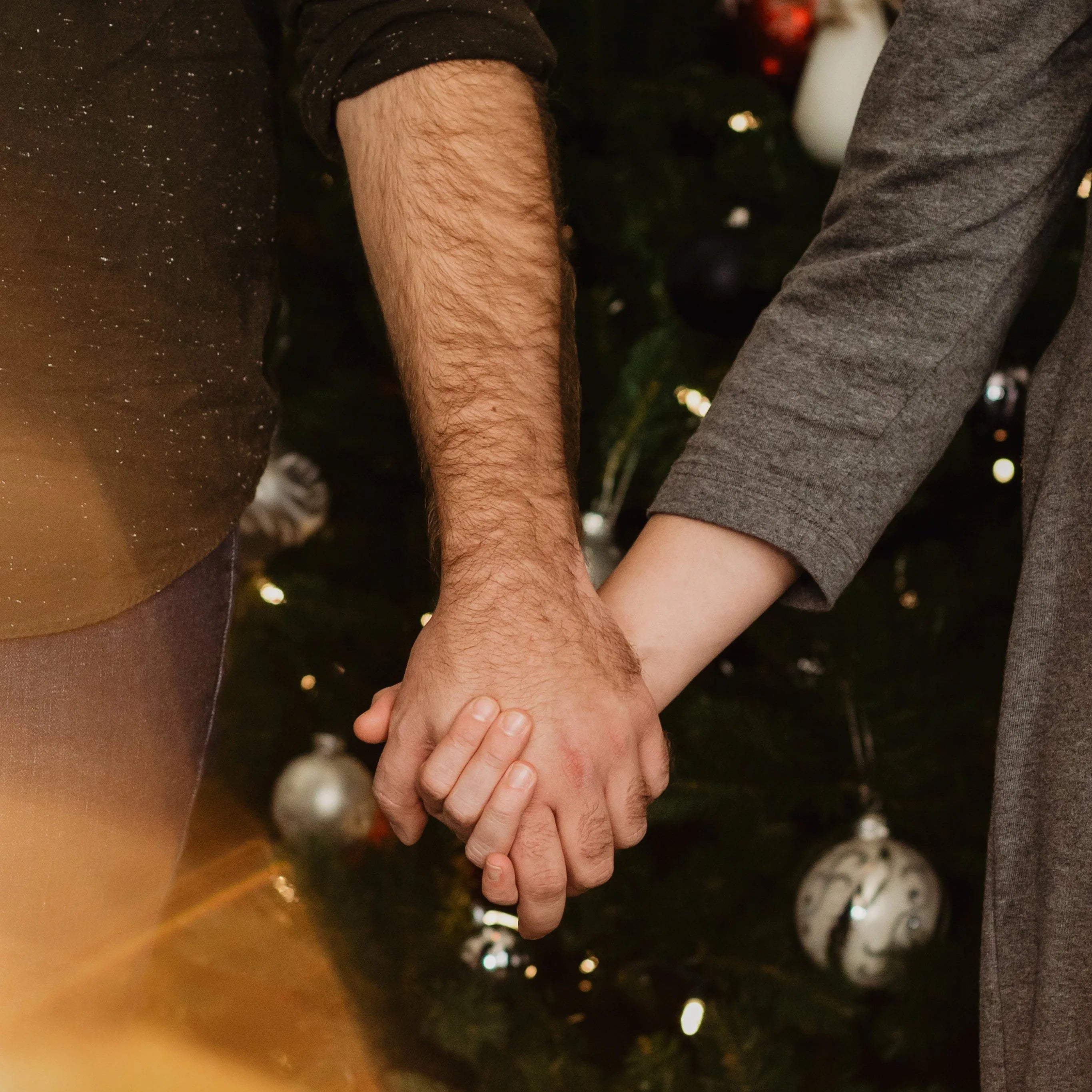 A couple holding hands by a Christmas tree during the holidays