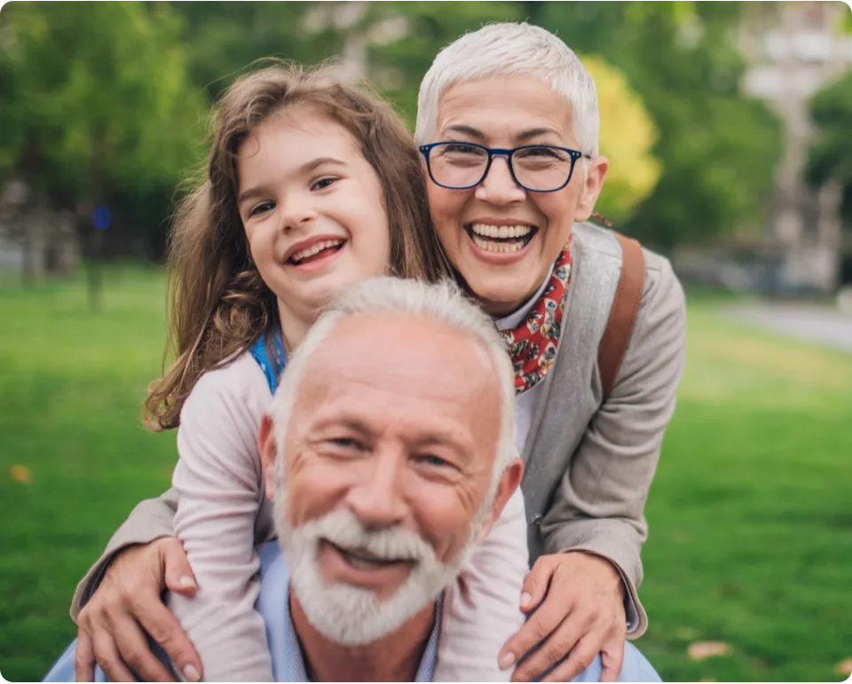 Grandparents smiling outdoors with their granddaughter