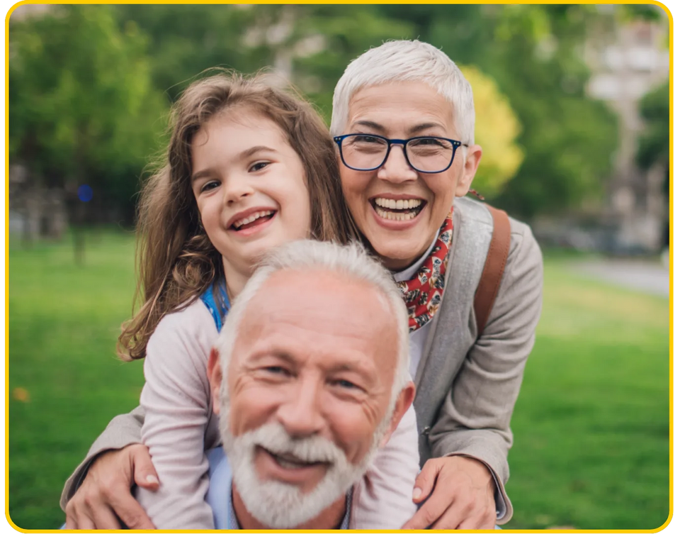 Grandparents smiling outdoors with their granddaughter